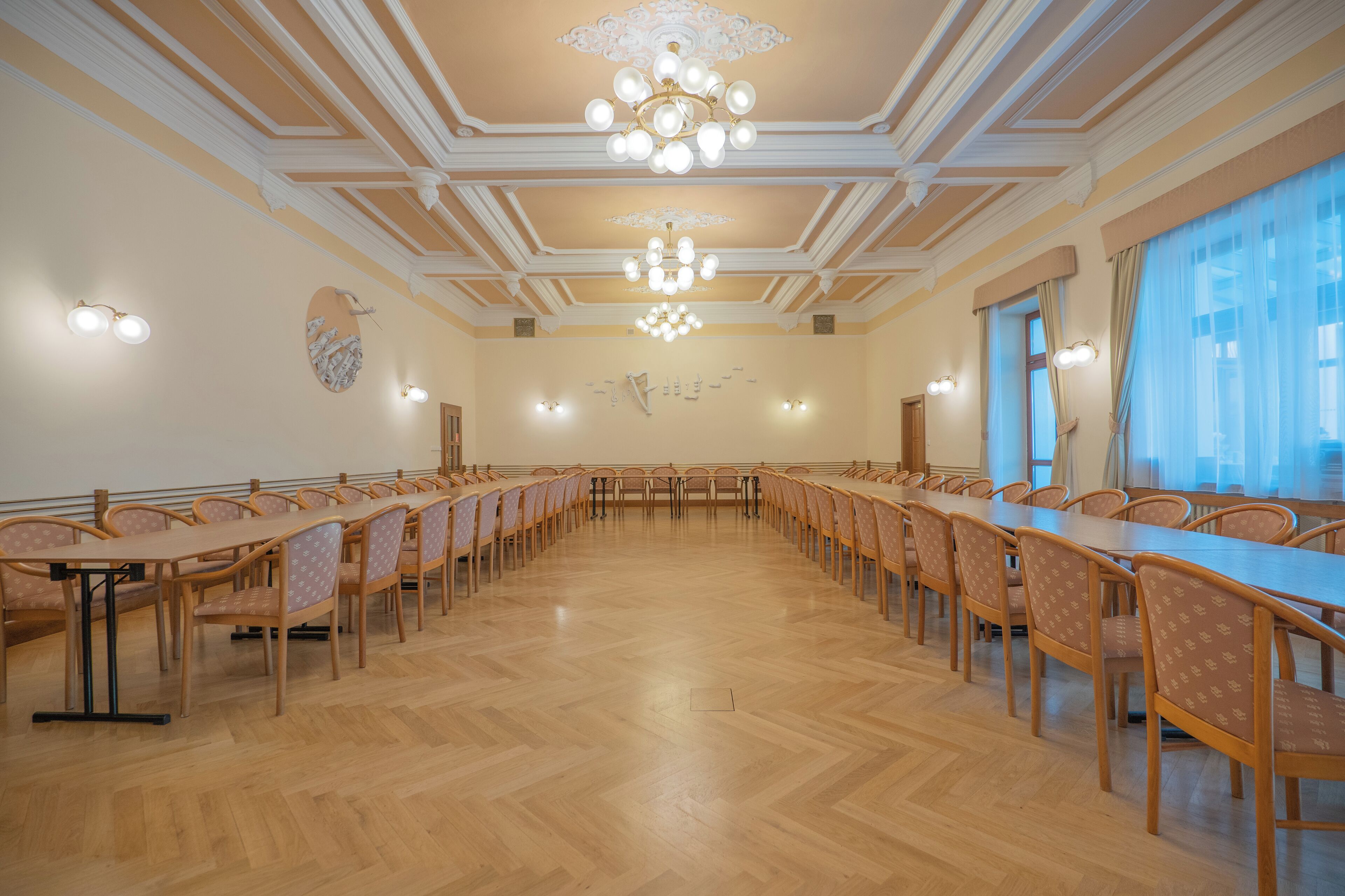 Una sala conferenze con un lungo tavolo e sedie, soffitto decorato e applique a parete.