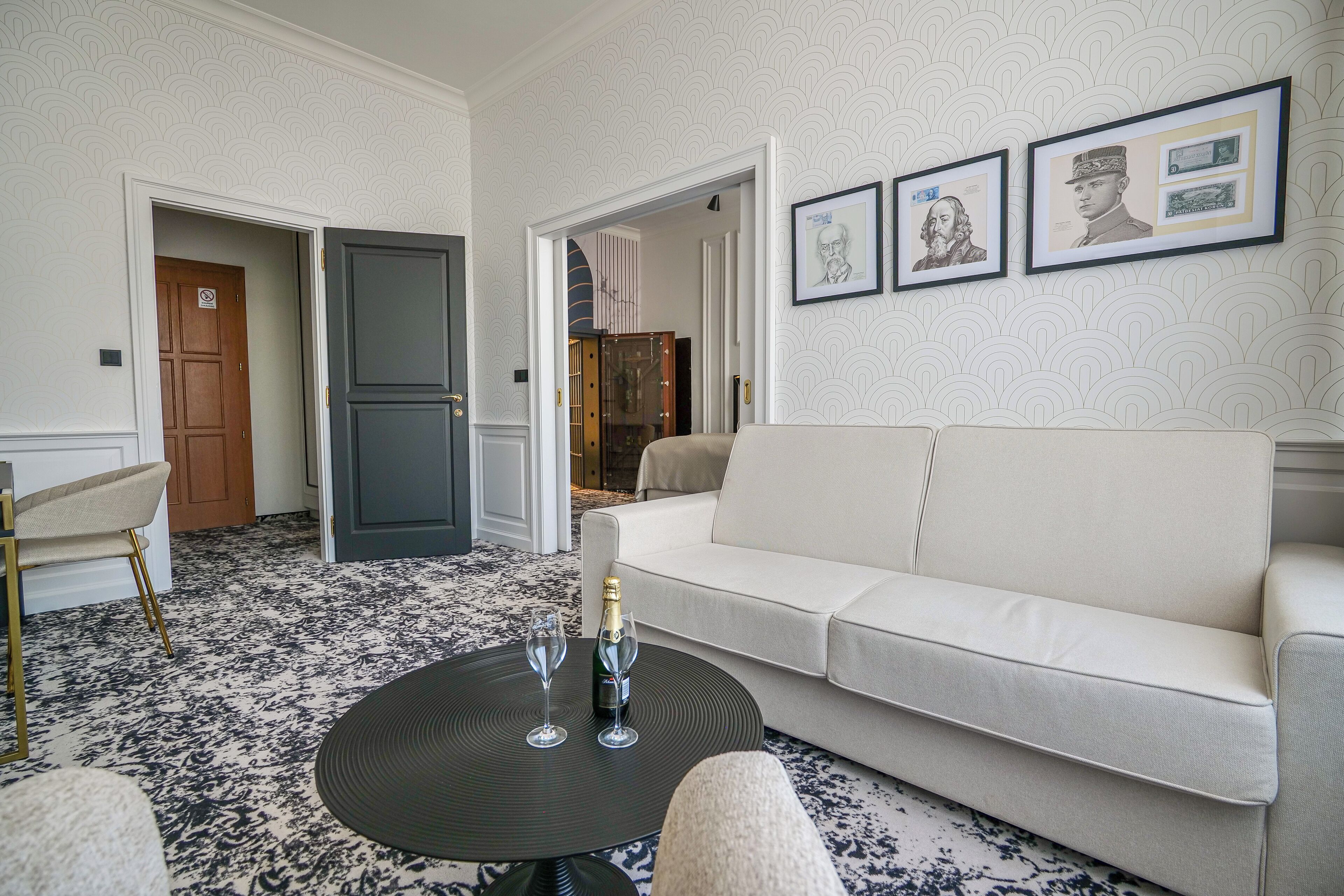 Uma sala de estar moderna com um sofá branco, uma mesa de centro redonda com dois copos e uma garrafa, e um tapete estampado.