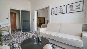 Uma sala de estar moderna com um sofá branco, uma mesa de centro redonda com dois copos e uma garrafa, e um tapete estampado.