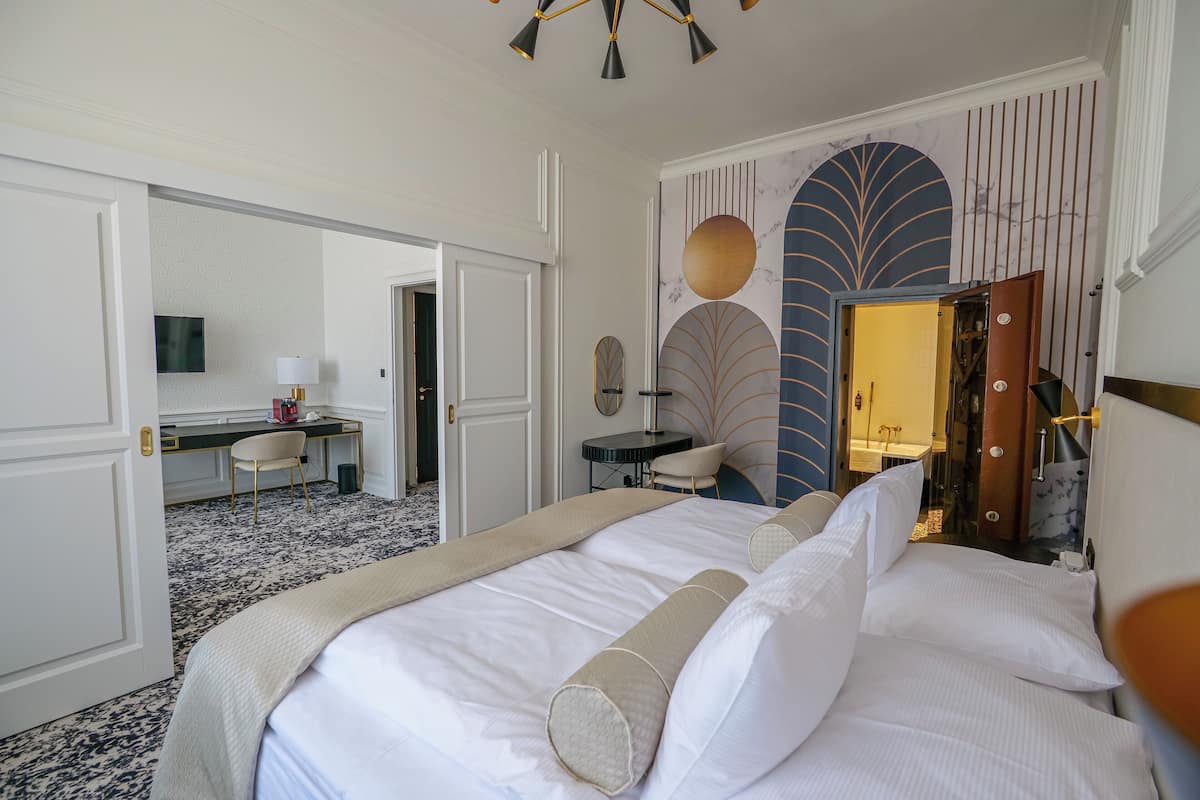 A hotel room with a large bed, a desk, a chair, and a bathroom visible through an open door.
