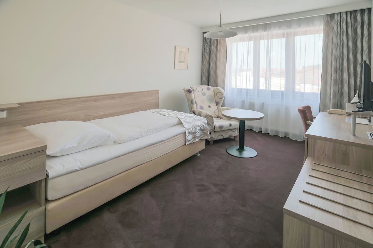 A hotel room with a bed, a chair, a small table, a desk, and a TV.