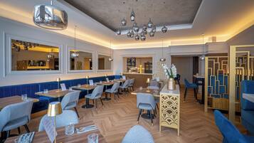 A modern restaurant with wooden flooring, blue upholstered seating, and pendant lighting.