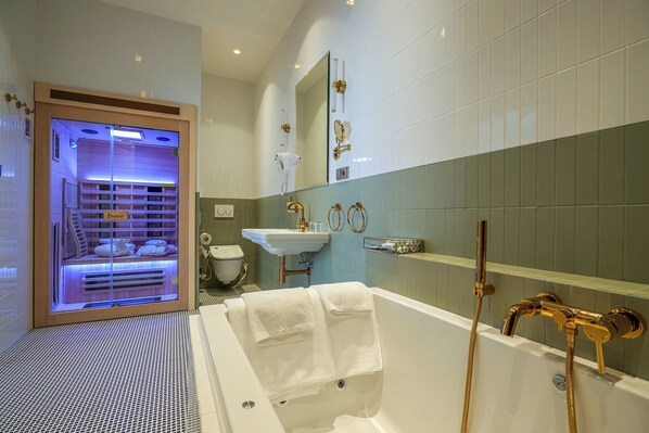 A modern bathroom with a glass-enclosed sauna, a white bathtub with gold fixtures, and a sink with a mirror above it. - Hotel Zlatá Hvězda (Litomysl)