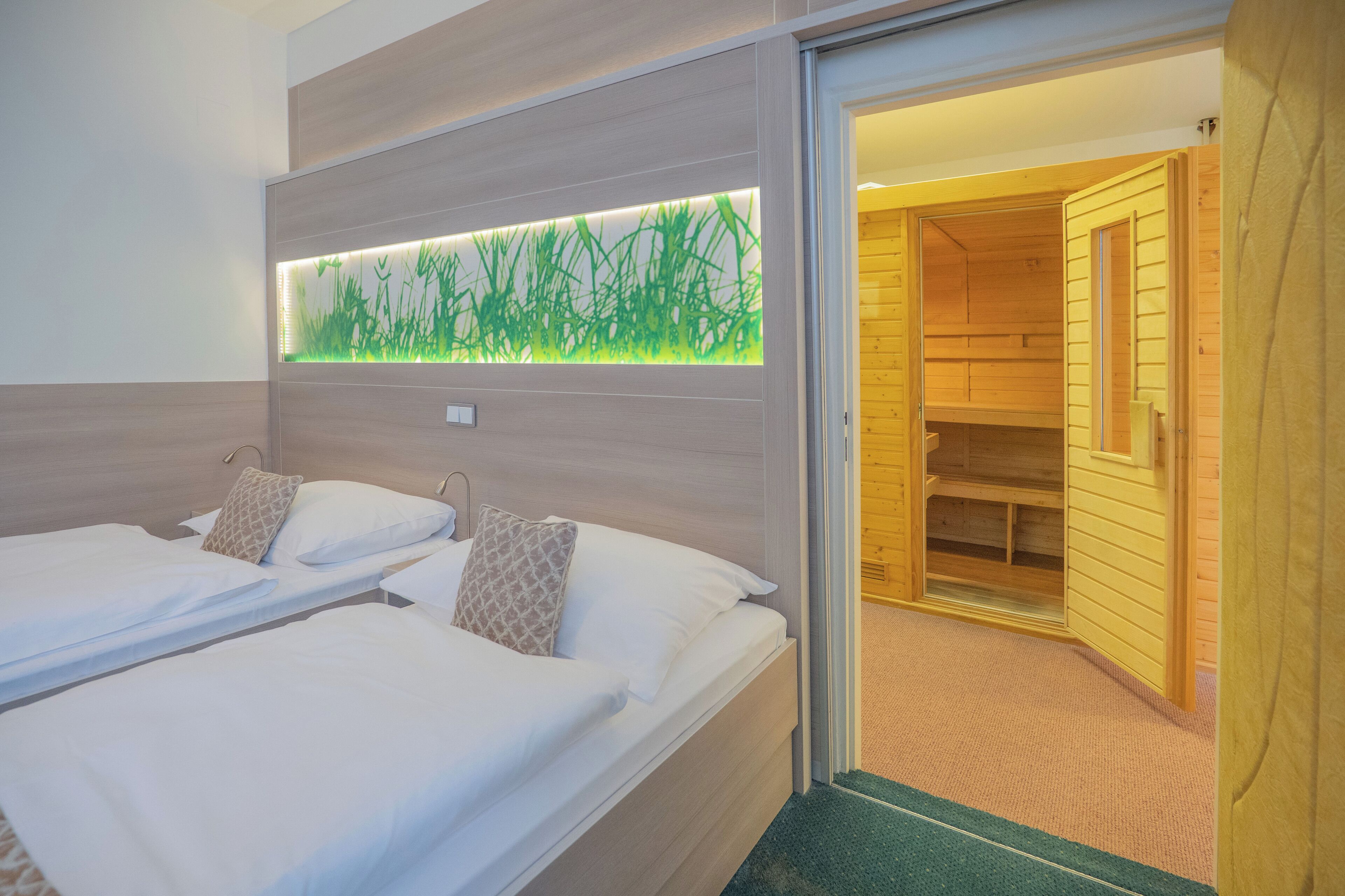 Une chambre d’hôtel avec deux lits, un panneau lumineux fixé au mur et un sauna en bois visible à travers une porte ouverte.