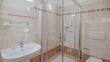 Bany amb dutxa tancada amb vidre, un lavabo amb productes de tocador i un vàter.