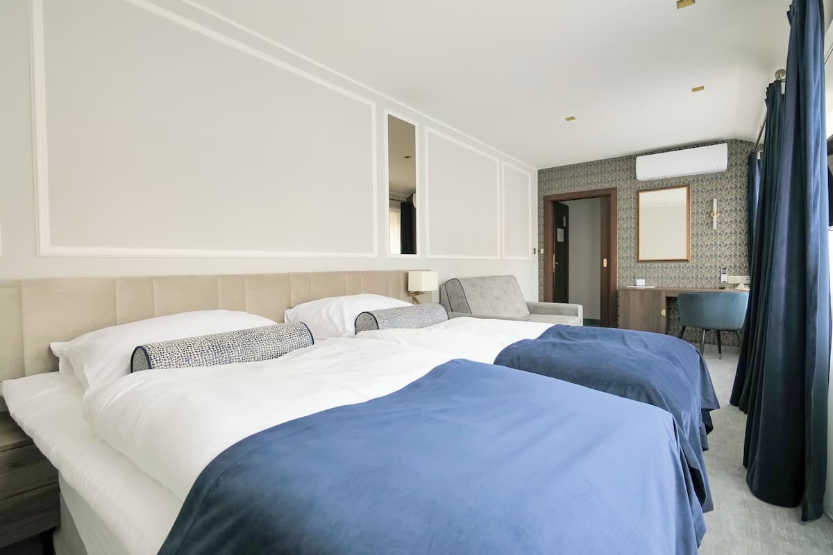 A hotel room with two beds, a desk, a chair, and a bathroom.