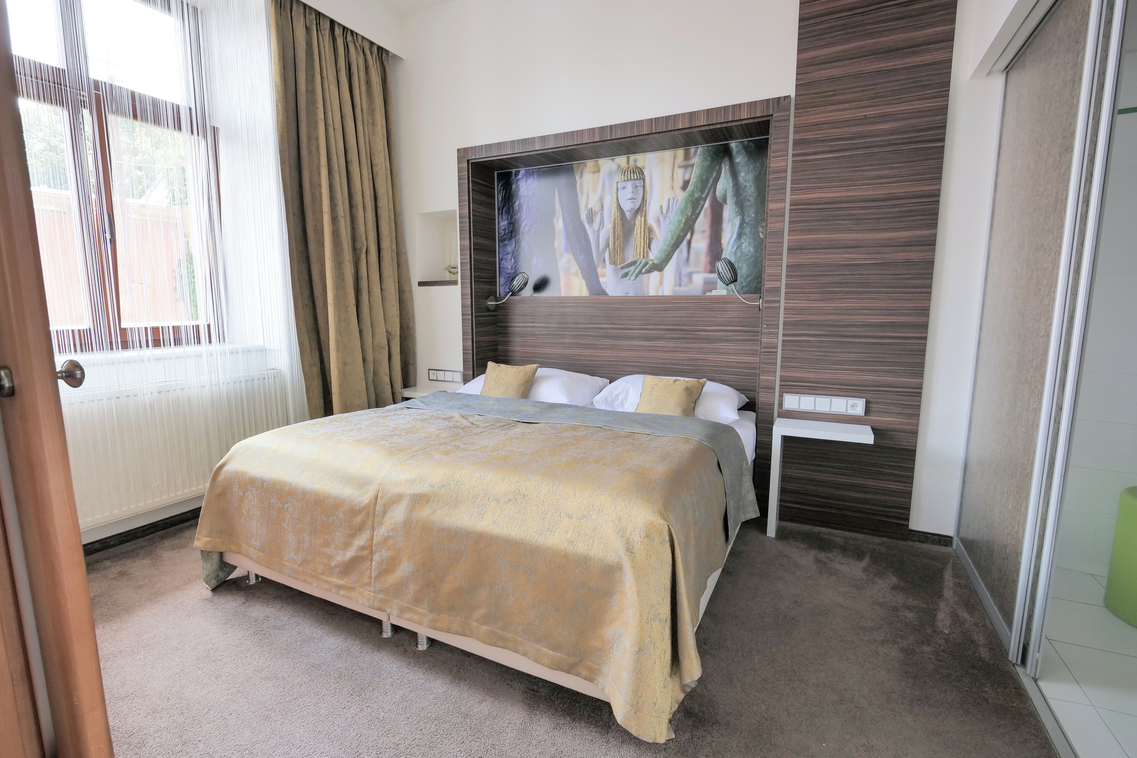 A bedroom with a bed, a painting on the wall, a window with curtains, and a radiator.
