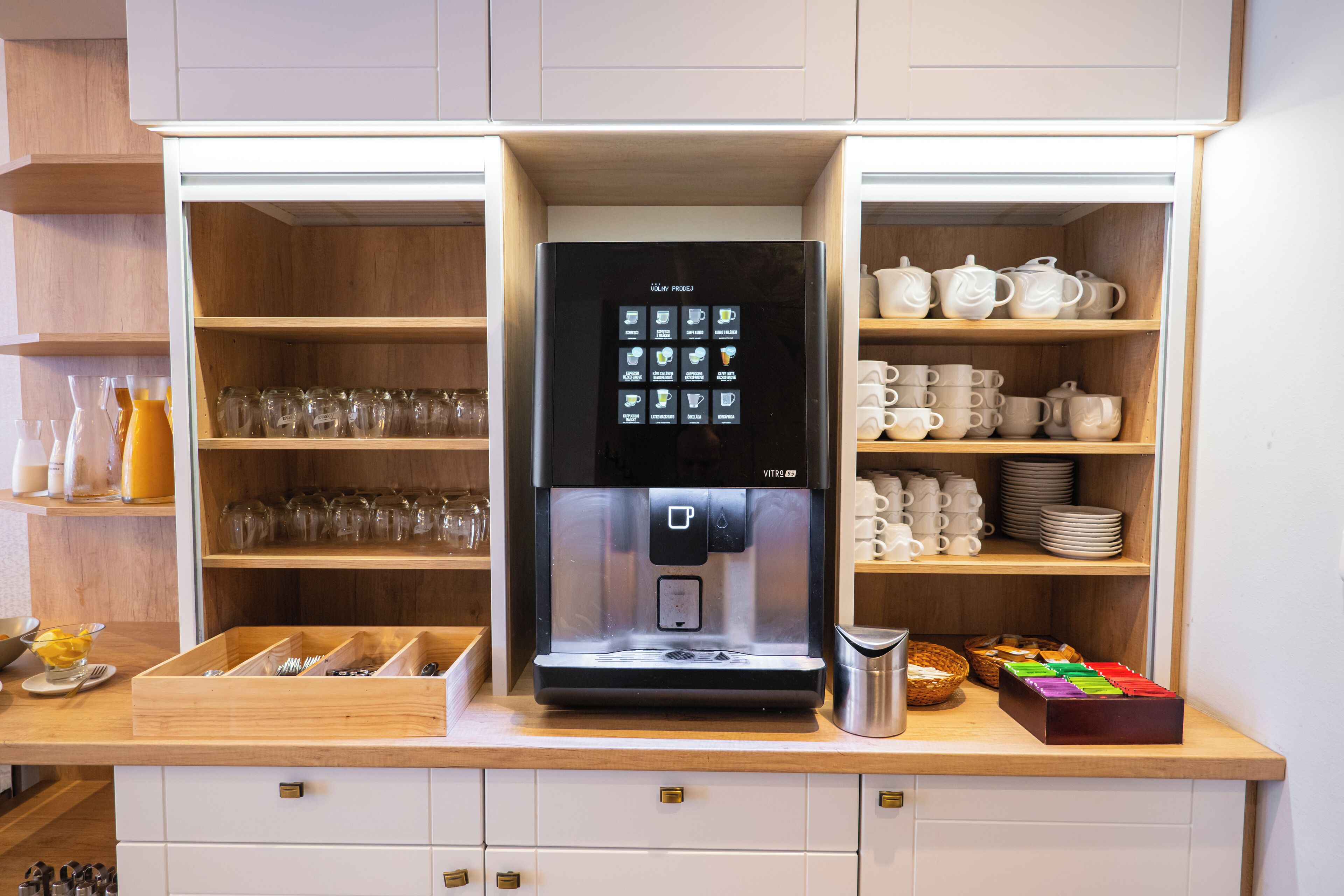 Une cuisine équipée d’un appareil à café intégré, d’étagères pour ranger la verrerie et d’un tiroir contenant des ustensiles de cuisine.