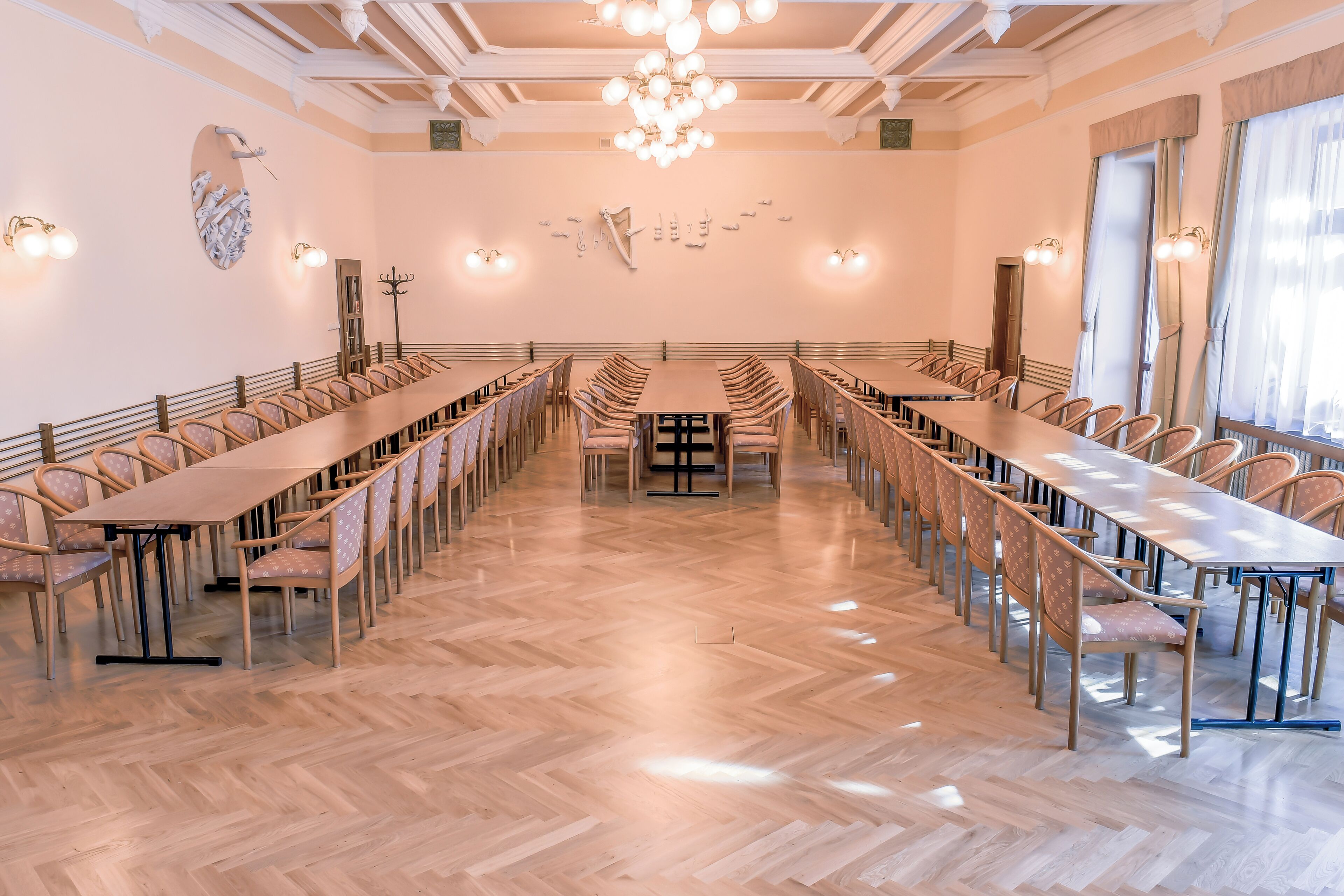 A conference room with a long table and chairs, wooden flooring, and wall-mounted lighting.