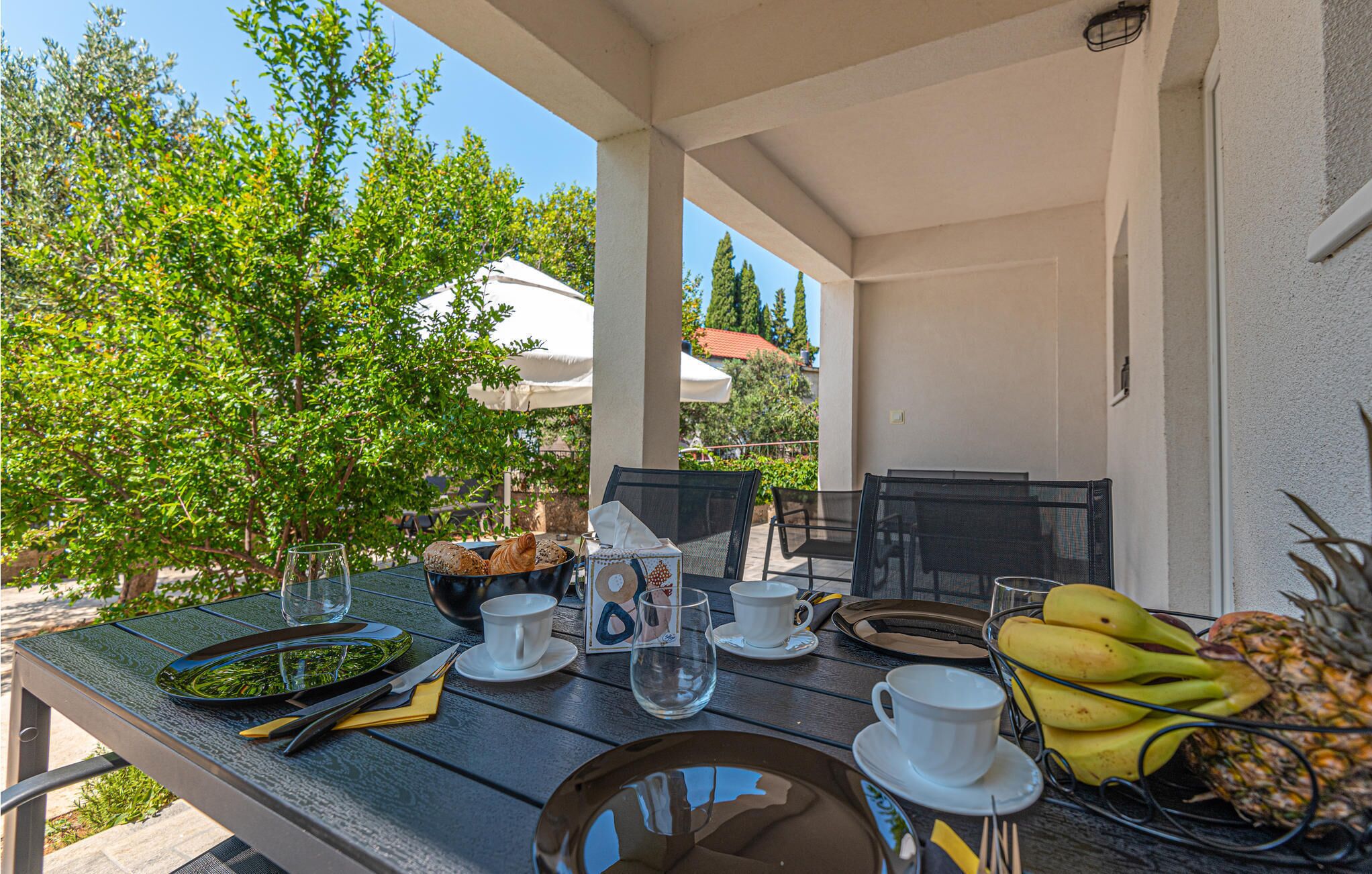 An outdoor dining area with a table set for two, including plates, cutlery, and cups.