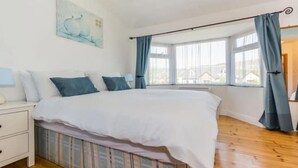 Een slaapkamer met een bed, nachtkastje, raam met gordijnen en een schilderij aan de muur.
