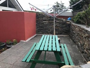 A green picnic table in a corner with a stone wall and a red building in the background. - 2 Marconi House, Apartment (Crookhaven)