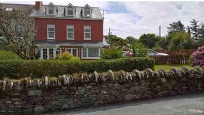 A two-story house with a stone wall in front, a red exterior, and a car parked nearby. - 3 Marconi House, Apartment (Crookhaven)
