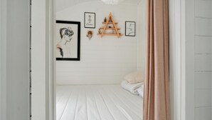 A bedroom with a white bed, a wooden shelf with decorative items, and framed artwork on the wall. - Stunning home in Askø with kitchen (Askø)