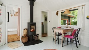 A cozy room with a wood-burning stove, a dining table with chairs, and a window with a view of greenery. - Stunning home in Askø with kitchen (Askø)