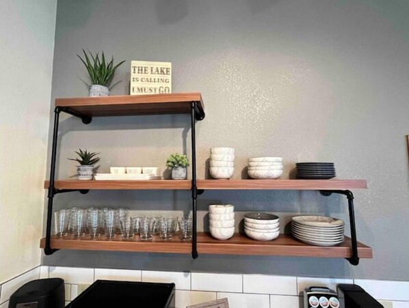 A kitchen shelf with glassware, bowls, and a sign that reads "THE LAKE IS CALLING I MUST GO".