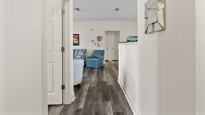 A hallway with a wooden floor, a blue armchair, a white door, and a wall-mounted mirror. - Ball fields! OWA! & Near the Beach! (Foley)