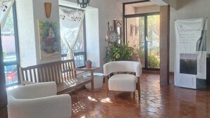 A spacious room with a tiled floor, a wooden bench, a white armchair, and a hanging light fixture. - Casa Maru Hotel (Parras)