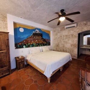 A bedroom with a bed, a wooden nightstand, a ceiling fan, a stone wall, and a mural on the wall. - Casa Maru Hotel (Parras)