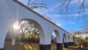 A white arched bridge with stone bases, surrounded by grass and trees, under a clear sky. - Casa Maru Hotel (Parras)