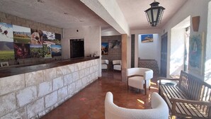 A lobby with a stone wall, a reception desk, and several seating areas with chairs and tables. - Casa Maru Hotel (Parras)