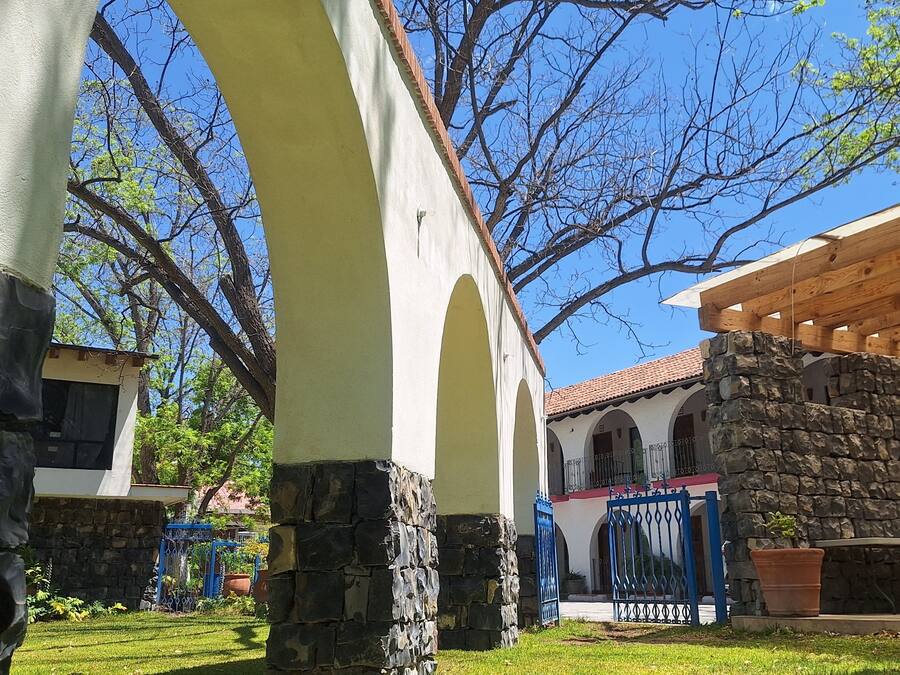 A courtyard with stone pillars, a wooden pergola, and a building with a tiled roof.
