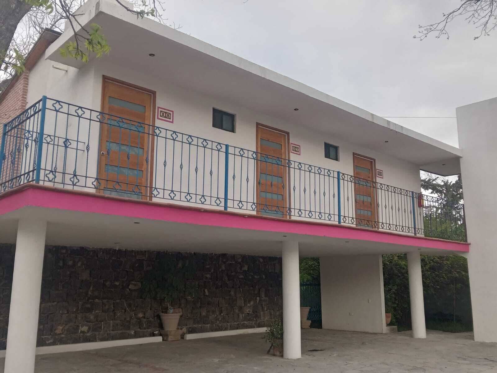 A two-story building with a balcony, stone wall, and potted plants.