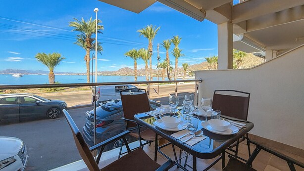 A balcony with a table set for dining, overlooking a coastal area with palm trees and a view of the ocean. - 2 bedroom amazing home in Cartagena (Cartagena)