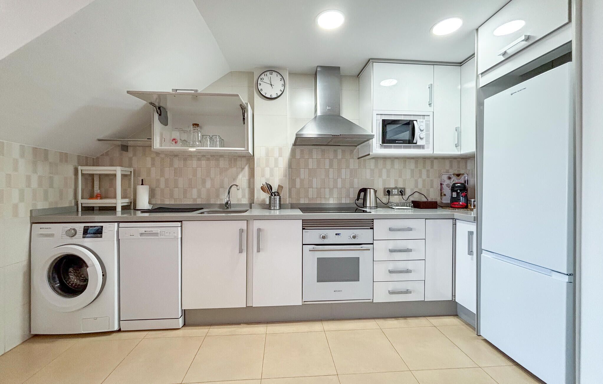 Een moderne keuken met witte kasten, een ingebouwde magnetron, een fornuis en een wasmachine.