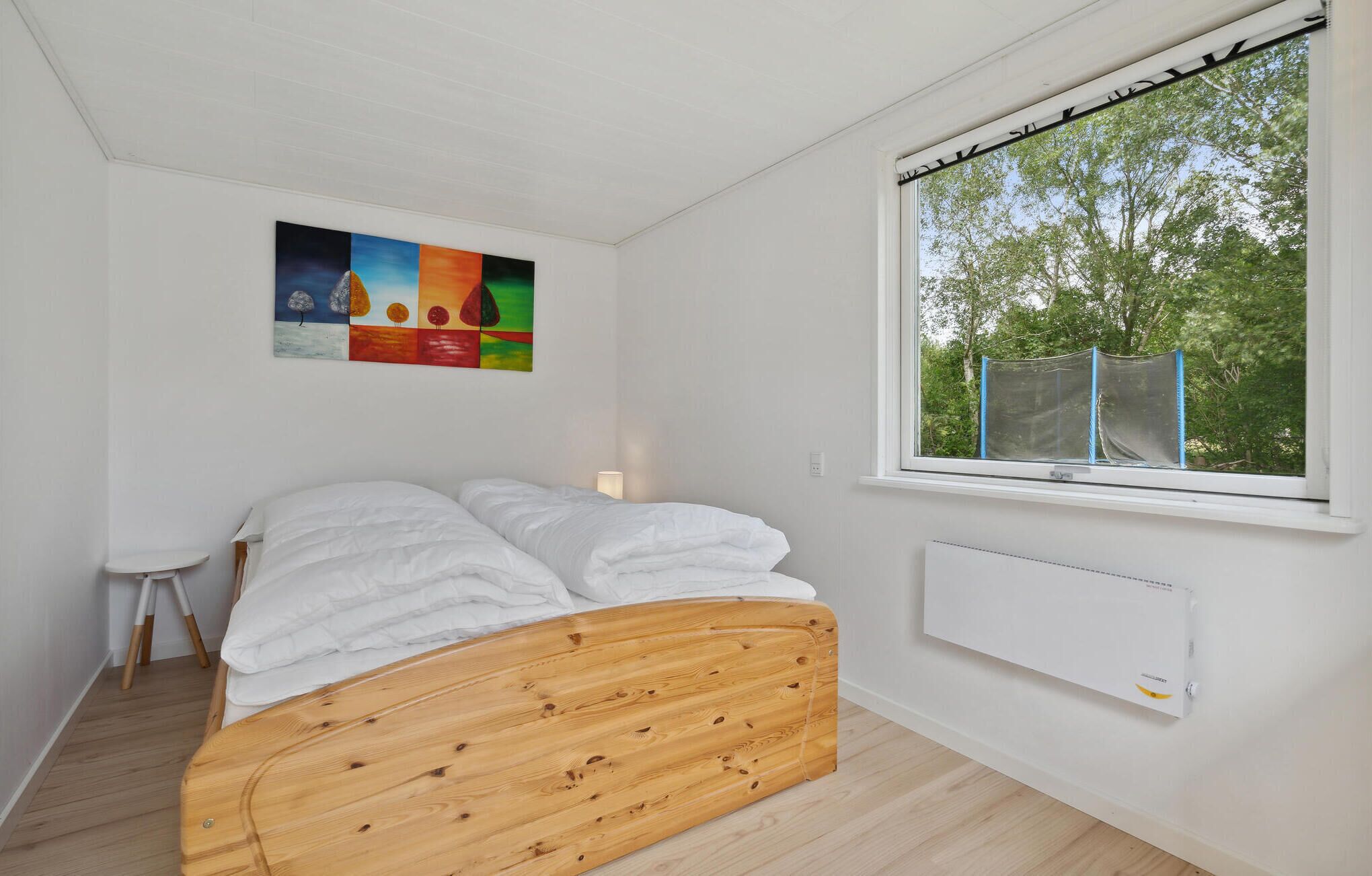 Een slaapkamer met een houten bed, een witte radiator en een raam met uitzicht op bomen.