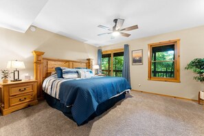 Ein Schlafzimmer mit Bett, Nachttisch, Lampe, Deckenventilator, Fenster mit Vorhängen und einer Pflanze.