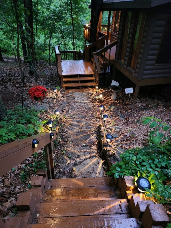 Una escalera de madera que lleva a una cabaña con terraza de madera y un arreglo floral rojo.