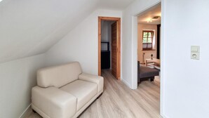 A modern loft bedroom with a sloped ceiling, a beige sofa, a wooden door, and a small table with a lamp. - Beautiful apartment in Kremmen with WiFi (Kremmen)