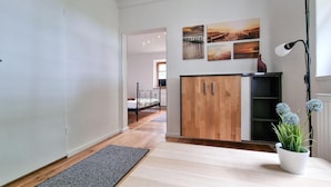 A hallway with a wooden cabinet, a black metal bed frame, a black rug, and a potted plant. - Beautiful apartment in Kremmen with WiFi (Kremmen)
