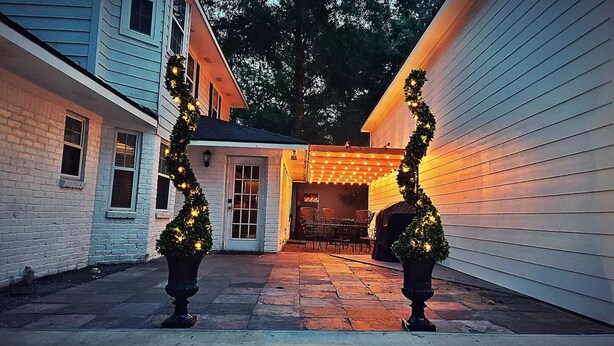 A patio area with a covered seating area, two potted Christmas trees, and a barbecue grill.