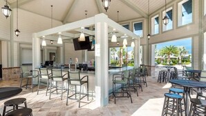 A spacious outdoor bar area with high ceilings and large windows, featuring multiple seating arrangements and a television screen. - Hidden Gem Jiminy Cricket (Kissimmee)