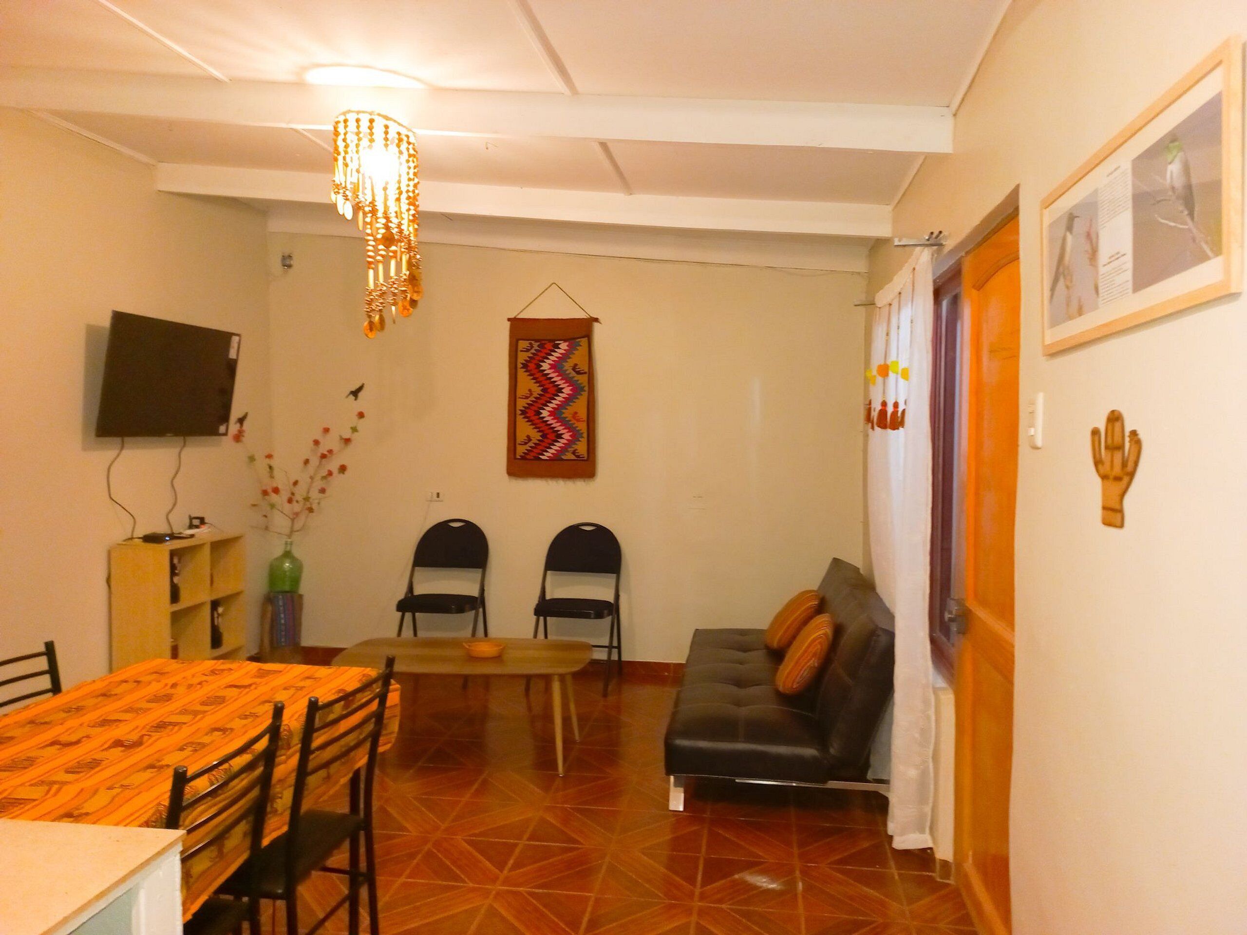 A dining area with a table, chairs, a sofa, a television, and a decorative wall hanging.