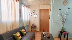 Ein Wohnzimmer mit einer Couch, einem Couchtisch mit einer Flasche und Gläsern, einer Holztür und einer Wanduhr.