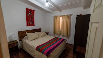 A bedroom with a wooden headboard, a bed with a striped blanket, a nightstand with a lamp, a red artwork on the wall, and a window with curtains.