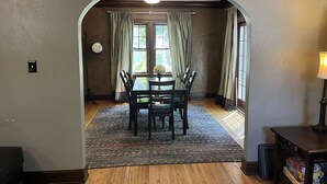 A dining area with a table and chairs, a rug, and curtains. - Historic Twin Tudors Inn Southwest Room (KP1404SW) (Sioux Falls)