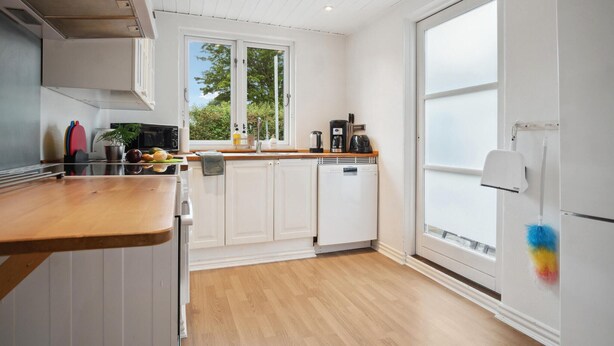 A modern kitchen with white cabinetry, a wooden countertop, and a view of greenery outside. - Nice apartment in Samsø with WiFi (Samsø)
