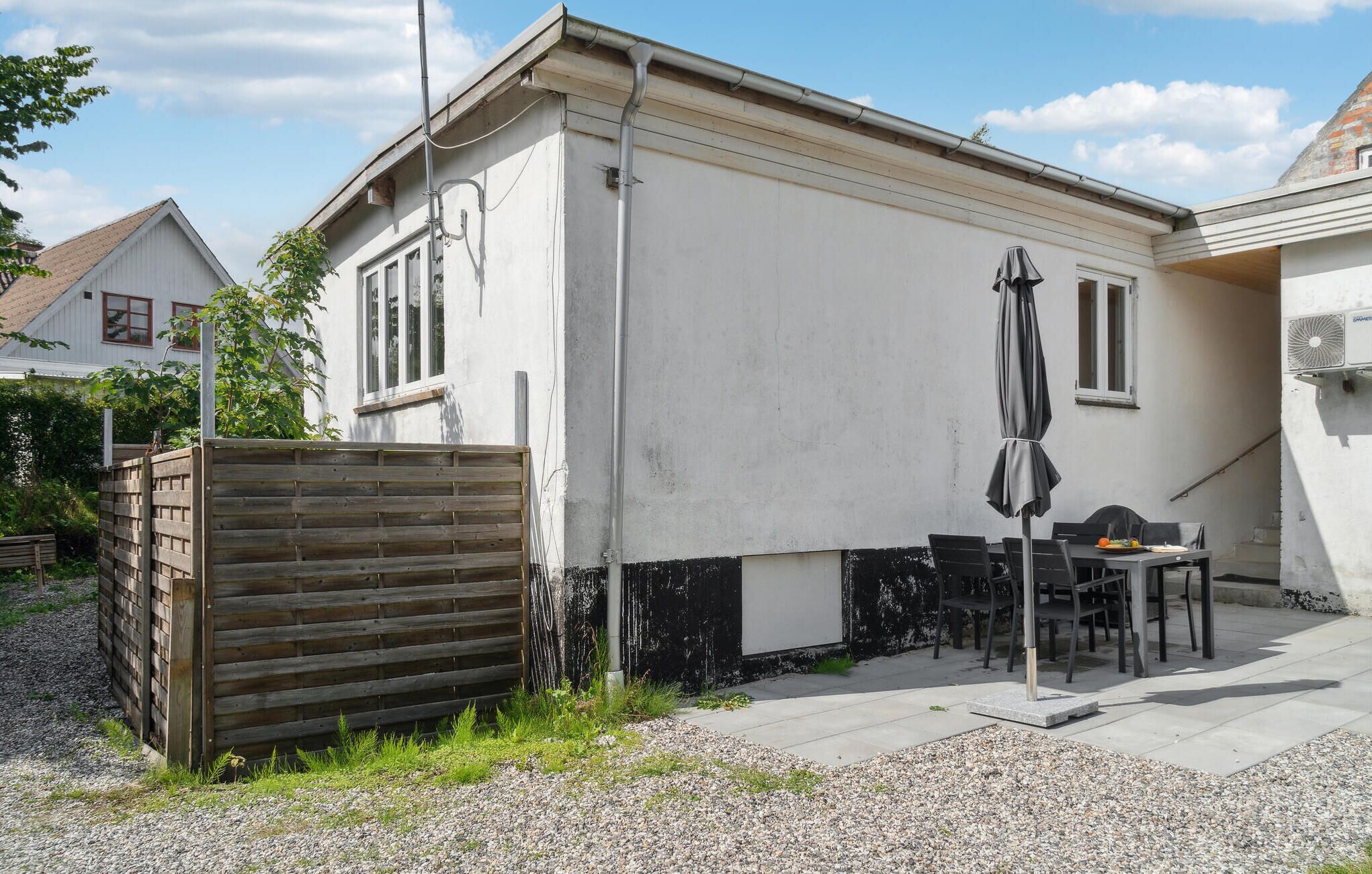 Ein kleines Gebäude mit Terrasse, Holzzaun und Gartenmöbeln.