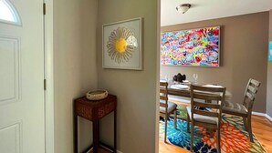 A dining area with a table set for four, a patterned rug, and a wall with a colorful abstract painting.