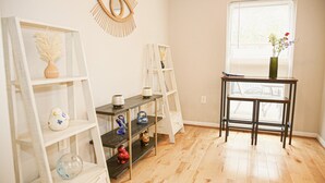 A room with wooden flooring, white and dark wooden shelves, a small table with a vase, and a window with blinds.