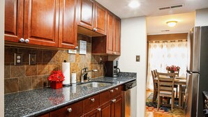 A kitchen with wooden cabinets, granite countertops, a coffee maker, and a refrigerator.