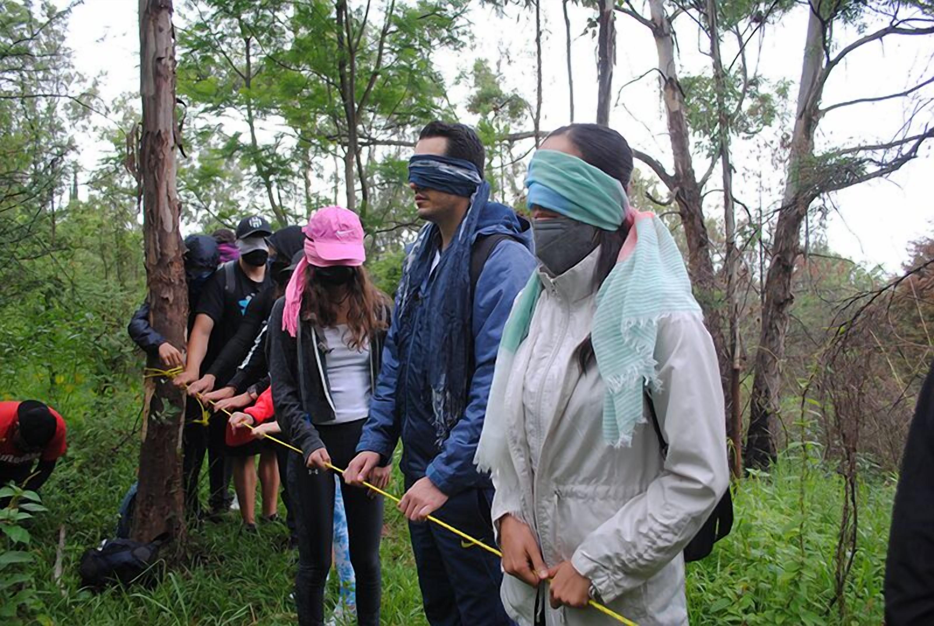 A group of people in a forested area, some wearing masks and bandanas, engaged in an outdoor activity.