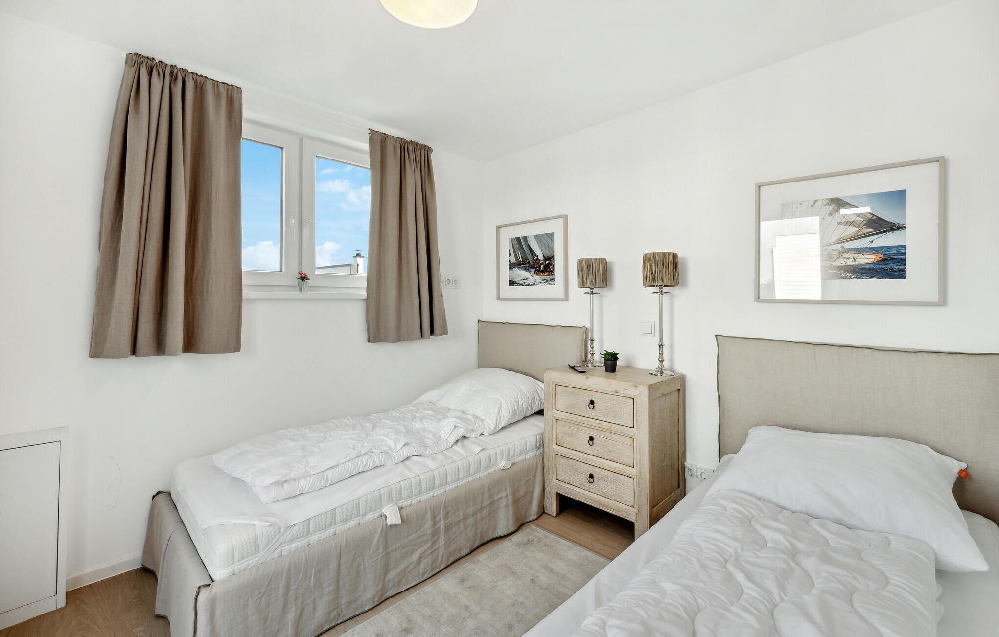 A bedroom with two single beds, a nightstand with a lamp, and two framed pictures on the wall.