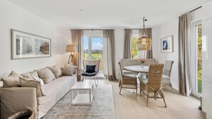 A spacious living room with a sofa, a dining table with chairs, a coffee table, and a view of the outdoors through large windows. - Cozy home in Tossens with sauna (Tossens)