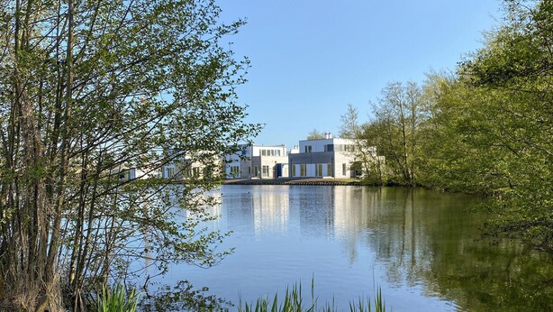 A lakeside property with modern architecture, a calm water body, and surrounding greenery. - Cozy home in Tossens with sauna (Tossens)