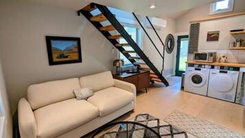 Un salon avec un canapé, un escalier, un lave-linge et un coin cuisine.